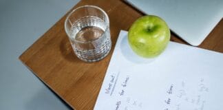 Zielone jabłko, szklanka wody i plan treningowy na drewnianym biurku