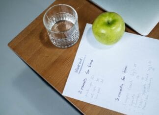 Jak zacząć zdrowy styl życia od zera: prosty plan zmian w diecie, ruchu i regeneracji Zielone jabłko, szklanka wody i plan treningowy na drewnianym biurku
