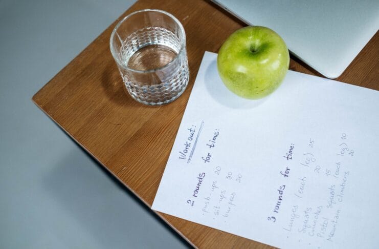 Zielone jabłko, szklanka wody i plan treningowy na drewnianym biurku